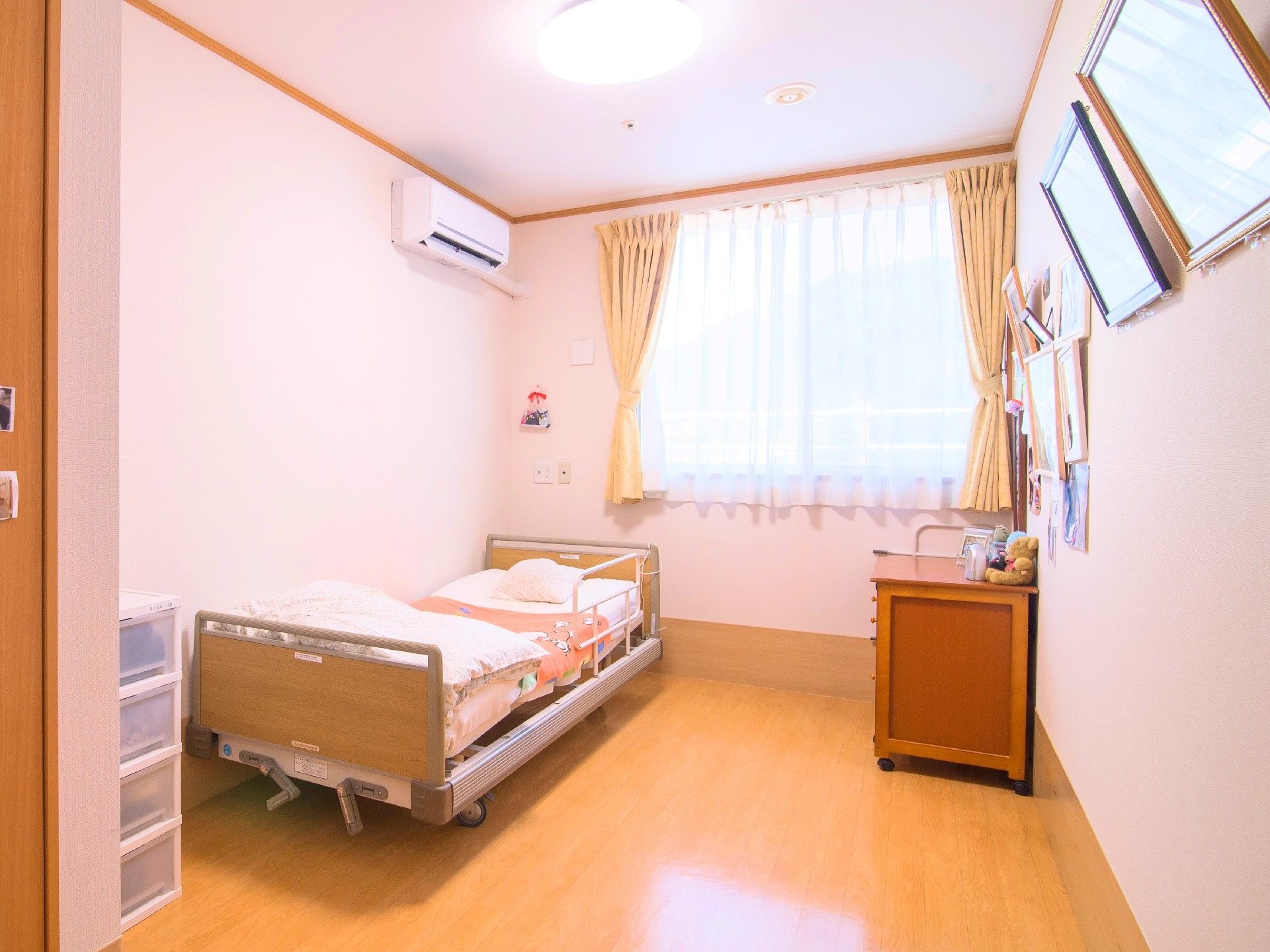 奥のほうに窓がある小さなワンルームタイプの部屋。エアコンやタンスなどがある部屋の様子
