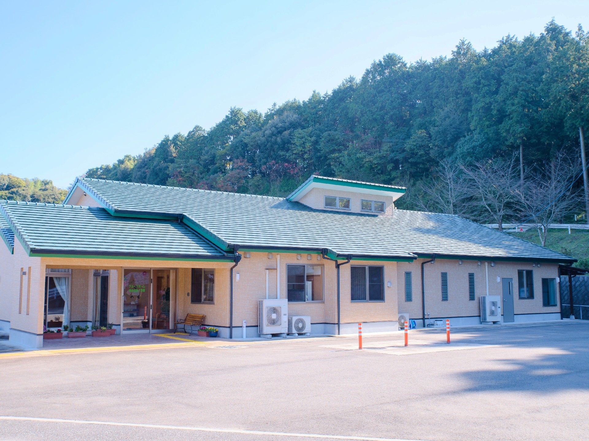 平屋建ての建物の写真。やわらかい色合いの建物が山に囲まれている様子