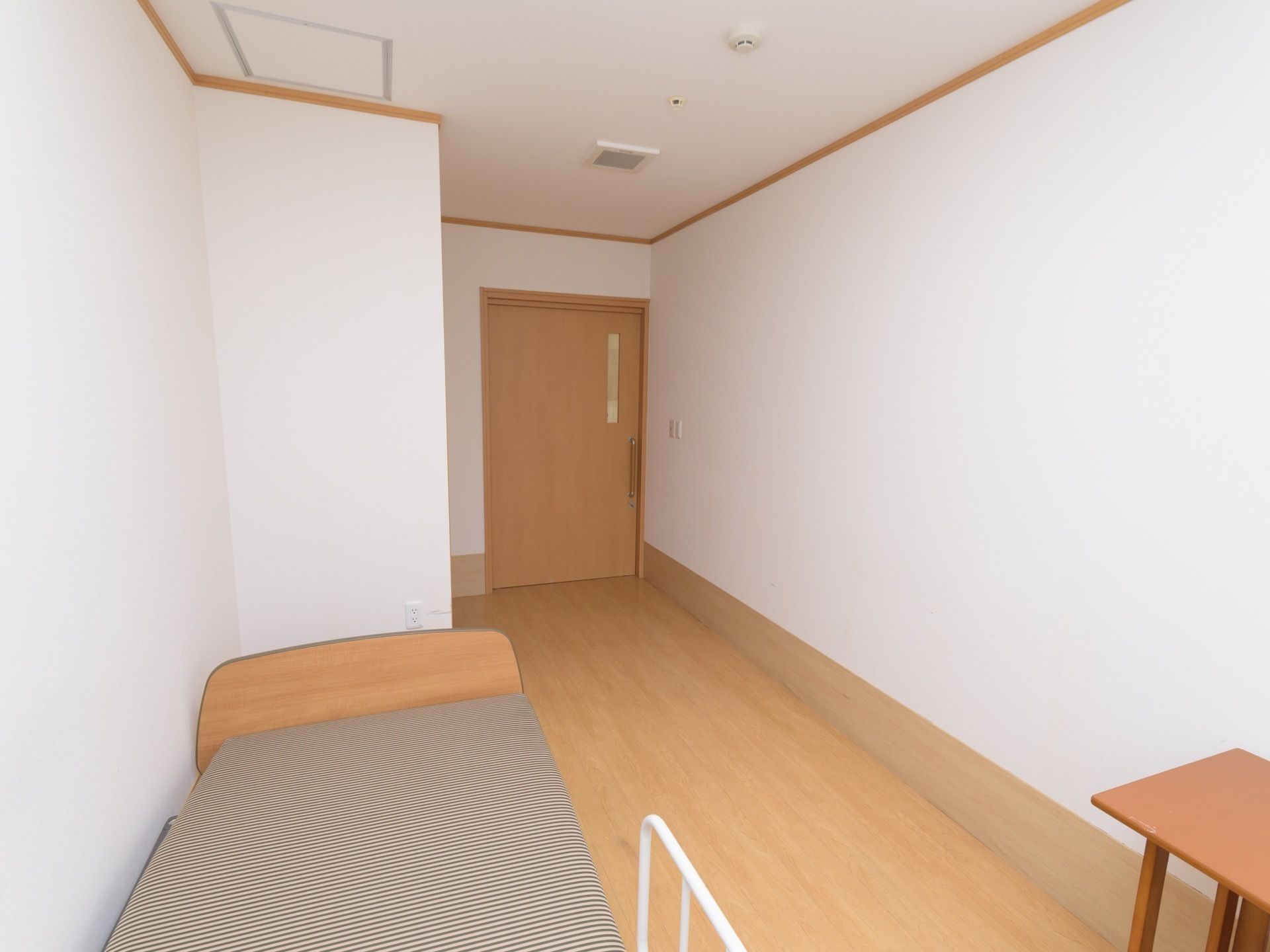 広めの間取りの居室である。介護ベッドと机が壁際に配置されている。出入り口の扉には、引き戸が採用されている。