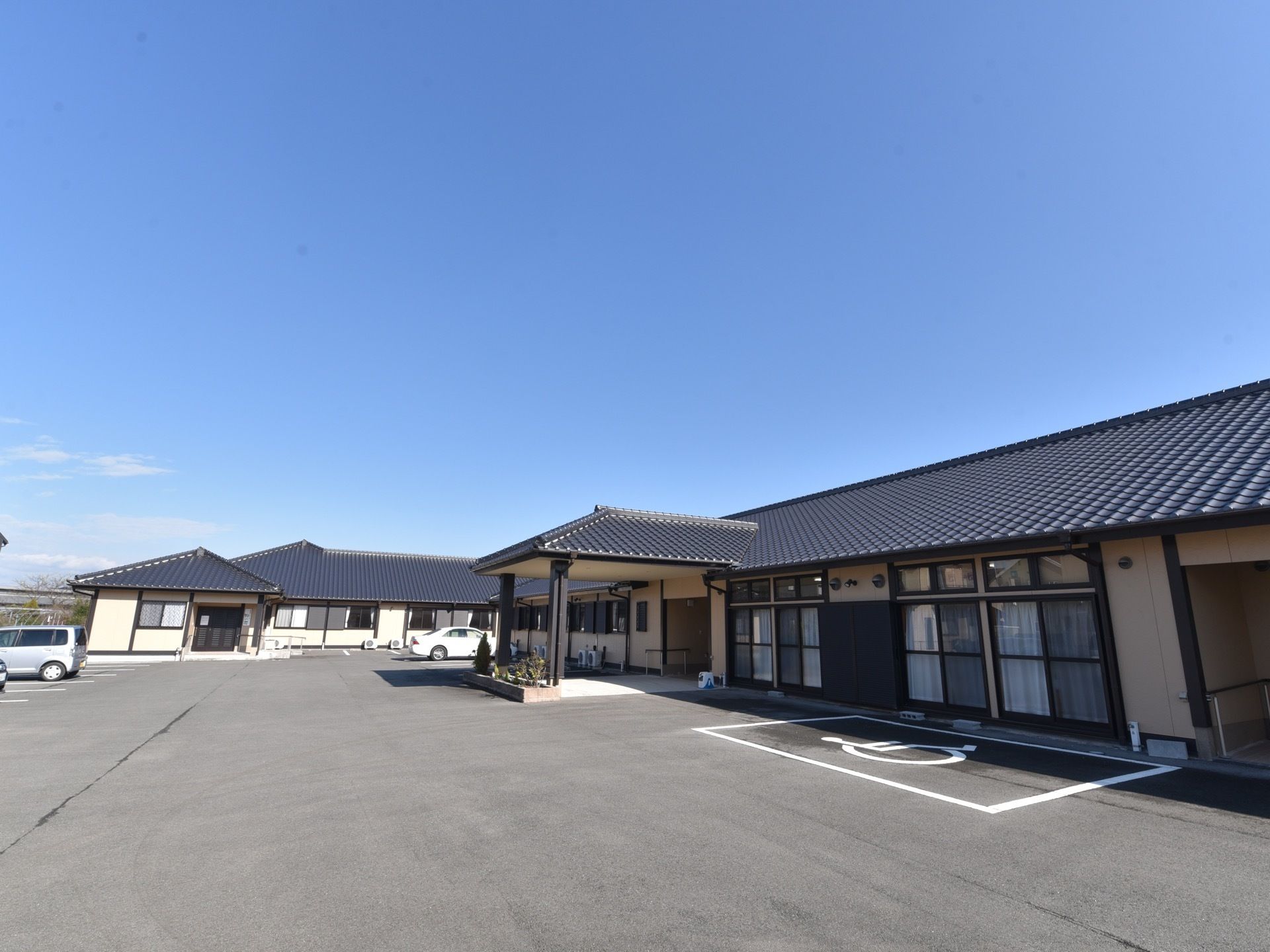 L字型の平屋建ての建物がある。日本家屋風の大きな瓦屋根になっている。周囲の地面は舗装され、駐車場になっている。