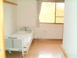 フローリングの白い布団がセットされた居室のベッドには手すりが付き、家具は置かれていないシンプルな部屋。
