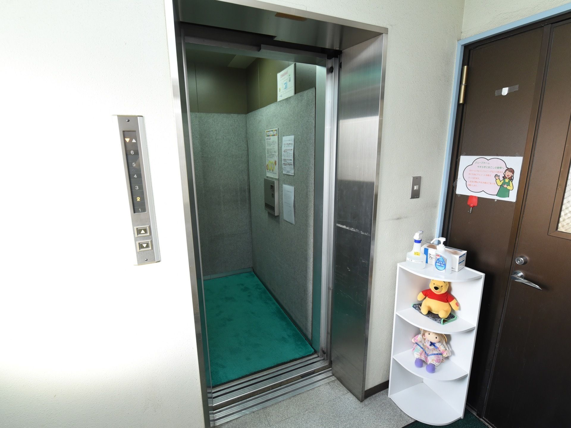 建物内にエレベーターが設置されている。ドアの前にコーナー用の棚が取りつけられ、ぬいぐるみが飾られている。