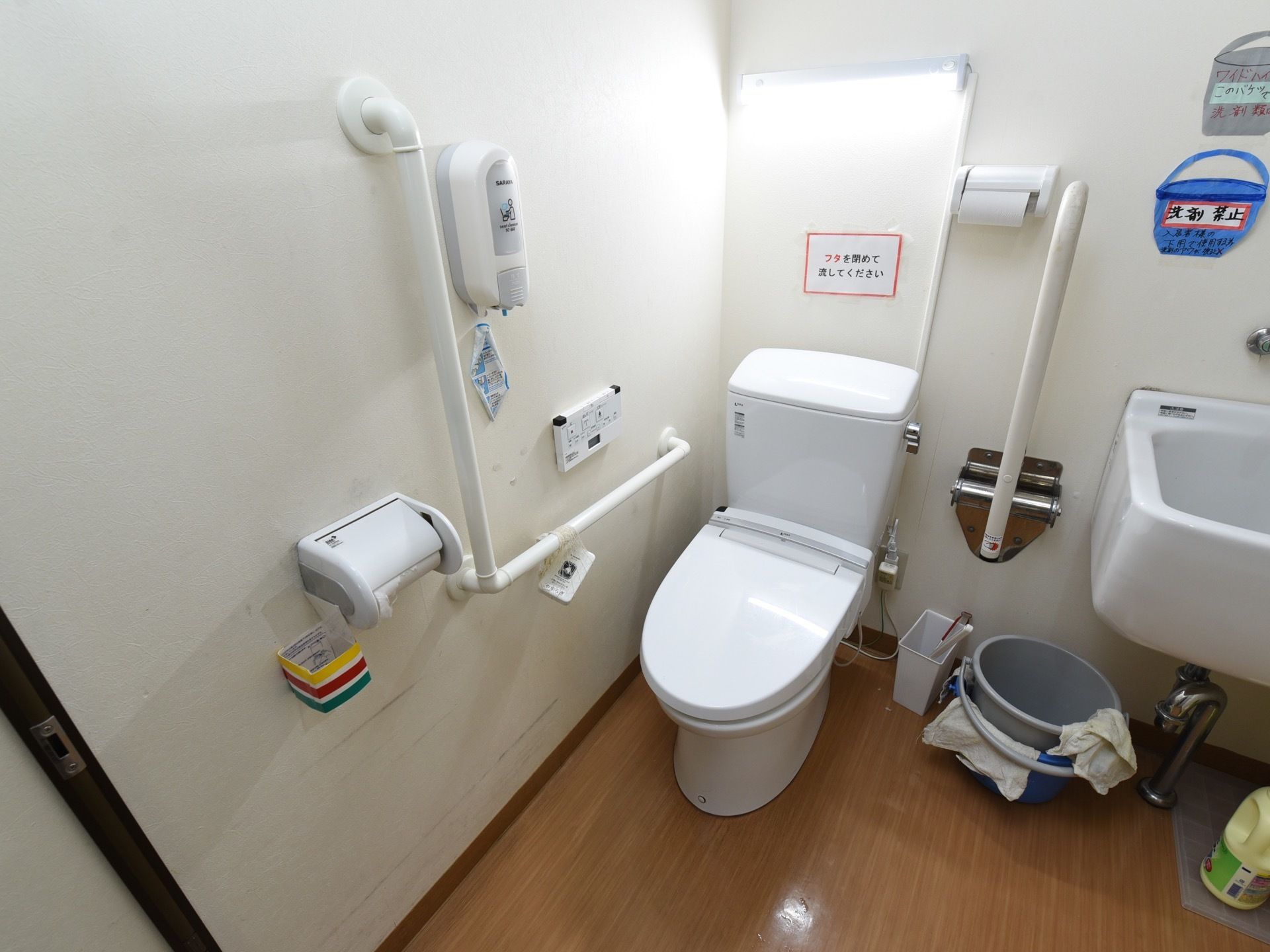 トイレには温水洗浄便座を取りつけている。壁に操作パネルとトイレットペーパー、手すりや消毒液が設置されている。