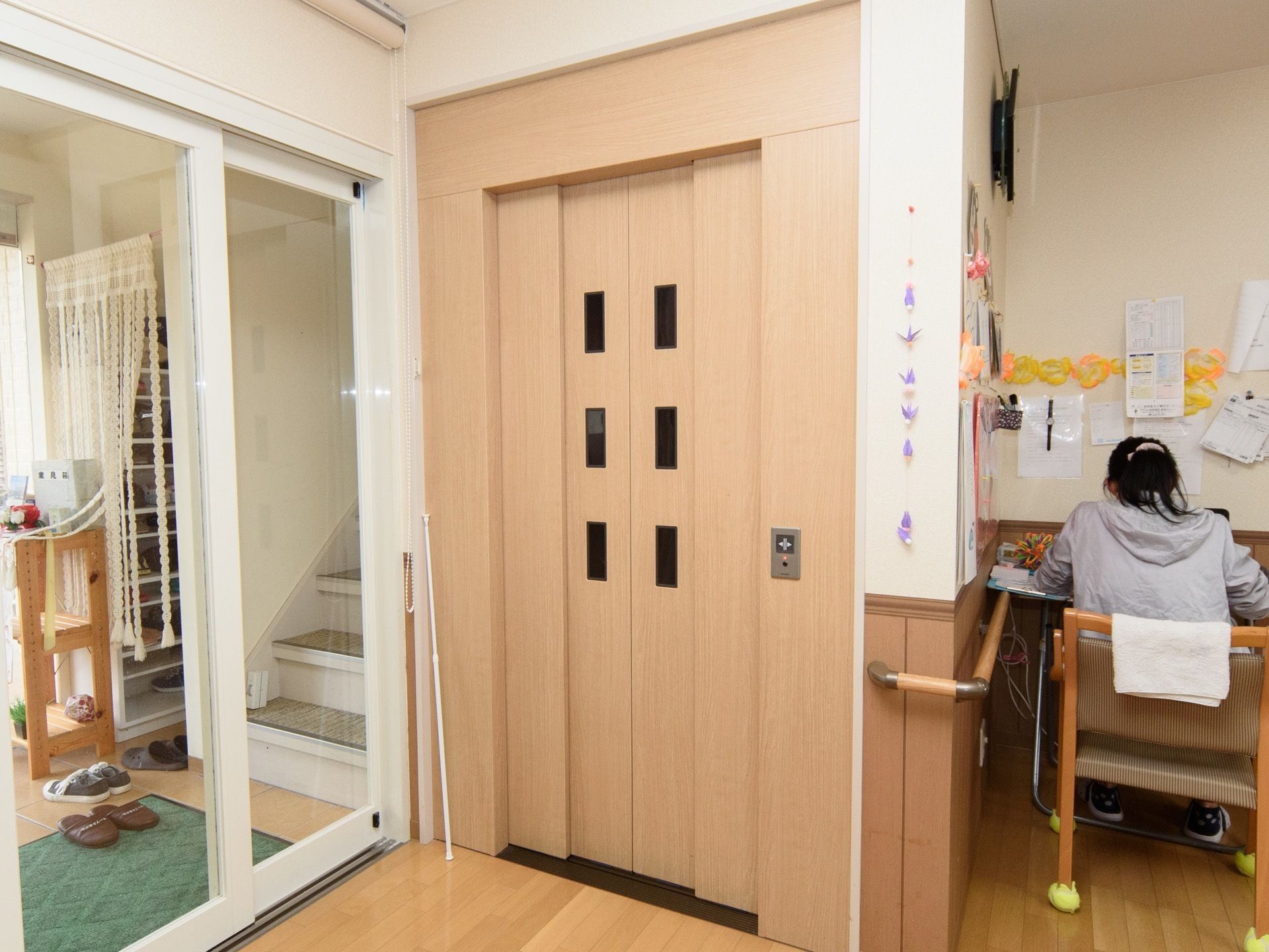 エレベーターの右側にデスクがあり、スタッフが座って作業を行っている。スタッフが座っている椅子にタオルが掛けられている。