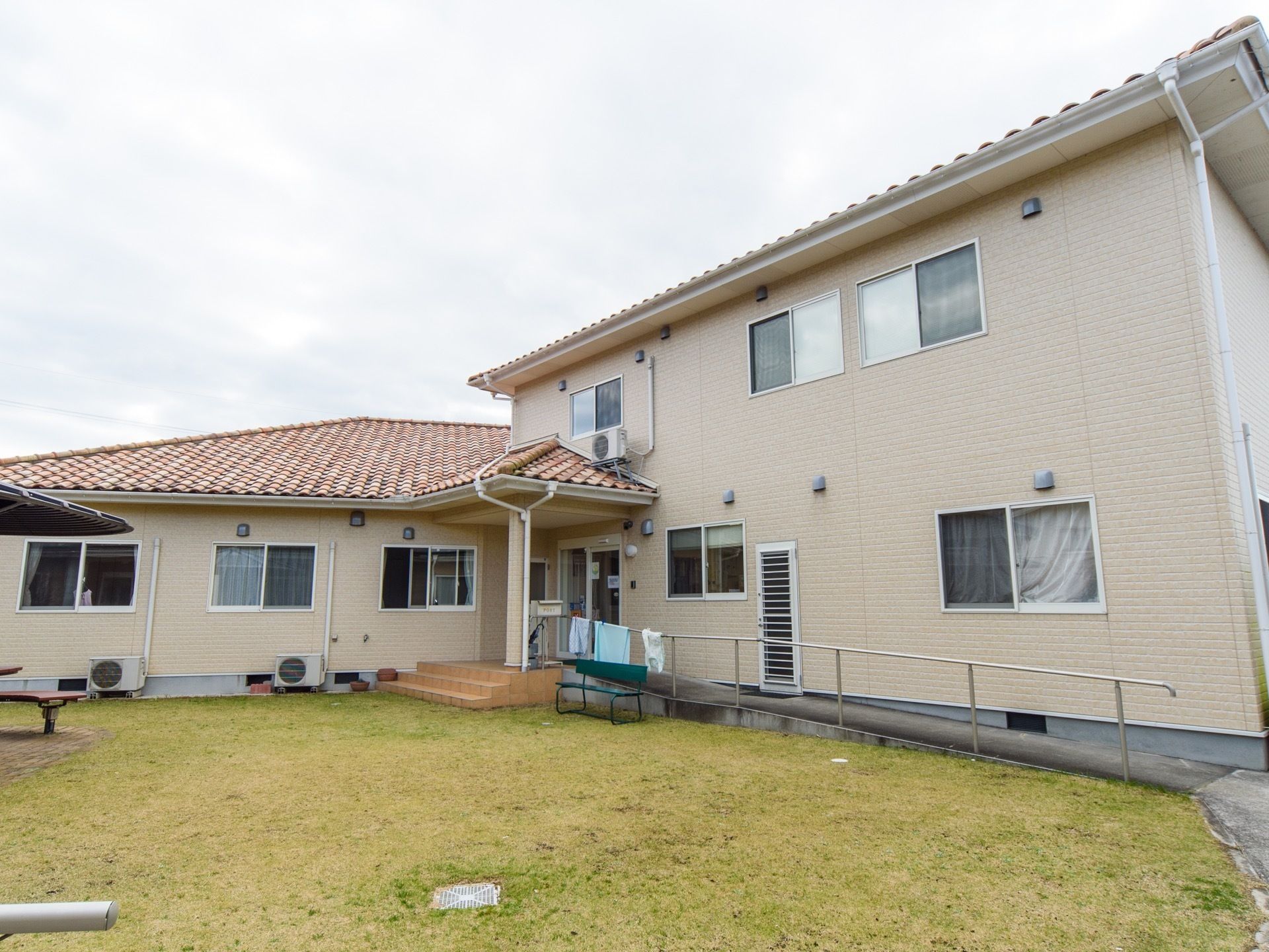 オレンジの瓦葺き２階建てである。出入口にはスロープと手すりが設けてある。芝生の庭にはベンチが置かれている。