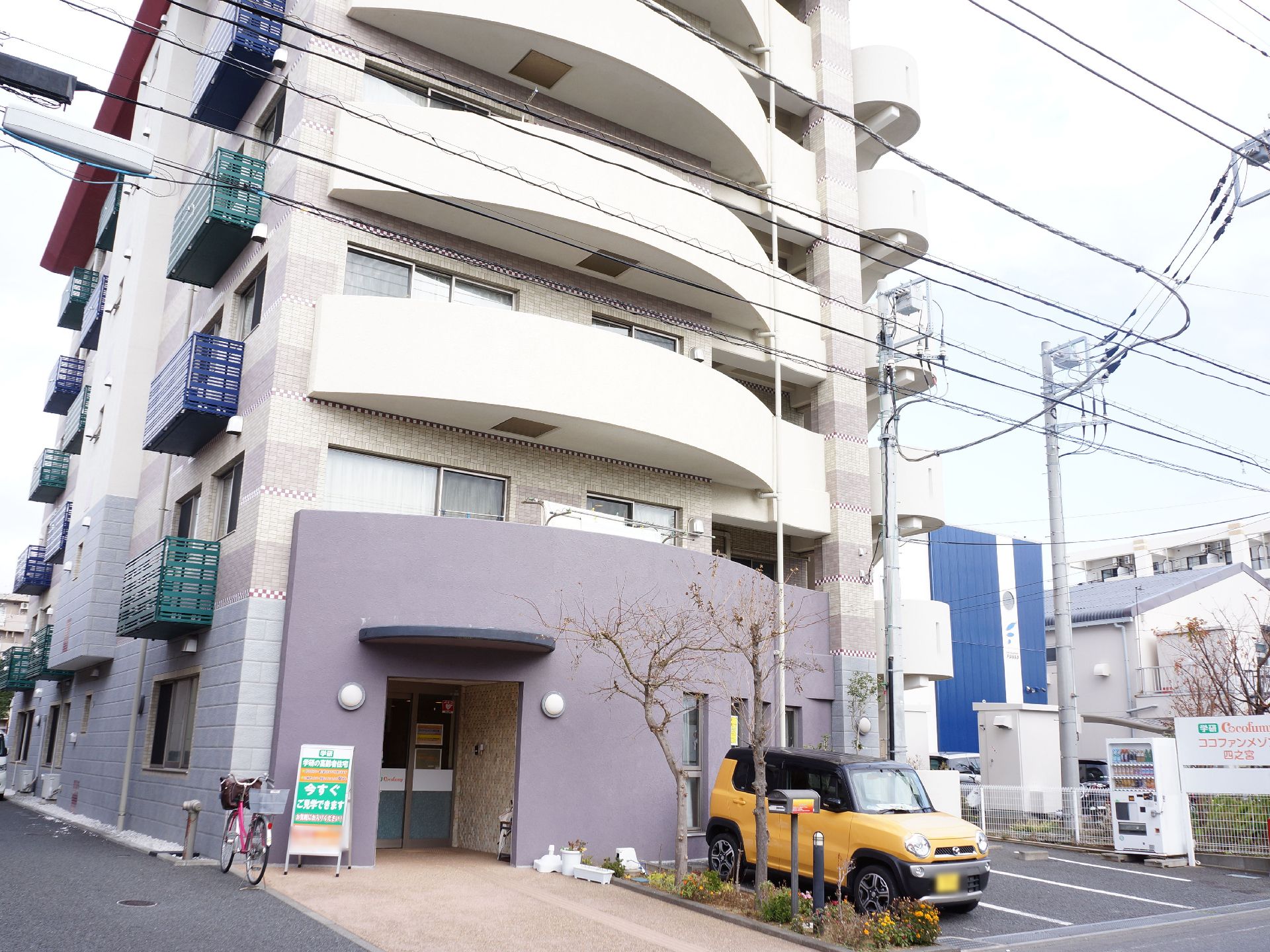 施設はベージュ色の六階建てで、前面には駐車スペースを設けている。玄関前には案内用の看板を設置している。