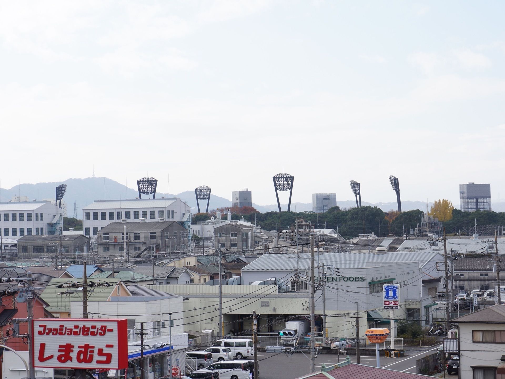 居室のベランダに出ると景色を広く見渡すことができる。近くにはコンビニエンスストアや衣料品店などがある。