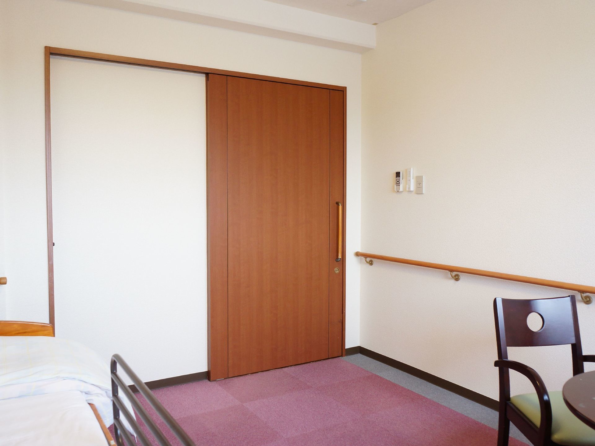 居室の入り口の扉は大きな握りハンドルを設置した引き戸である。壁には入り口付近から木製の手すりを取り付けている。