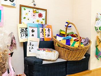 原っぱのような場所を笑顔で歩いているブラウンのジャケットを着た高齢女性と付き添いのエプロンを付けた女性スタッフ。