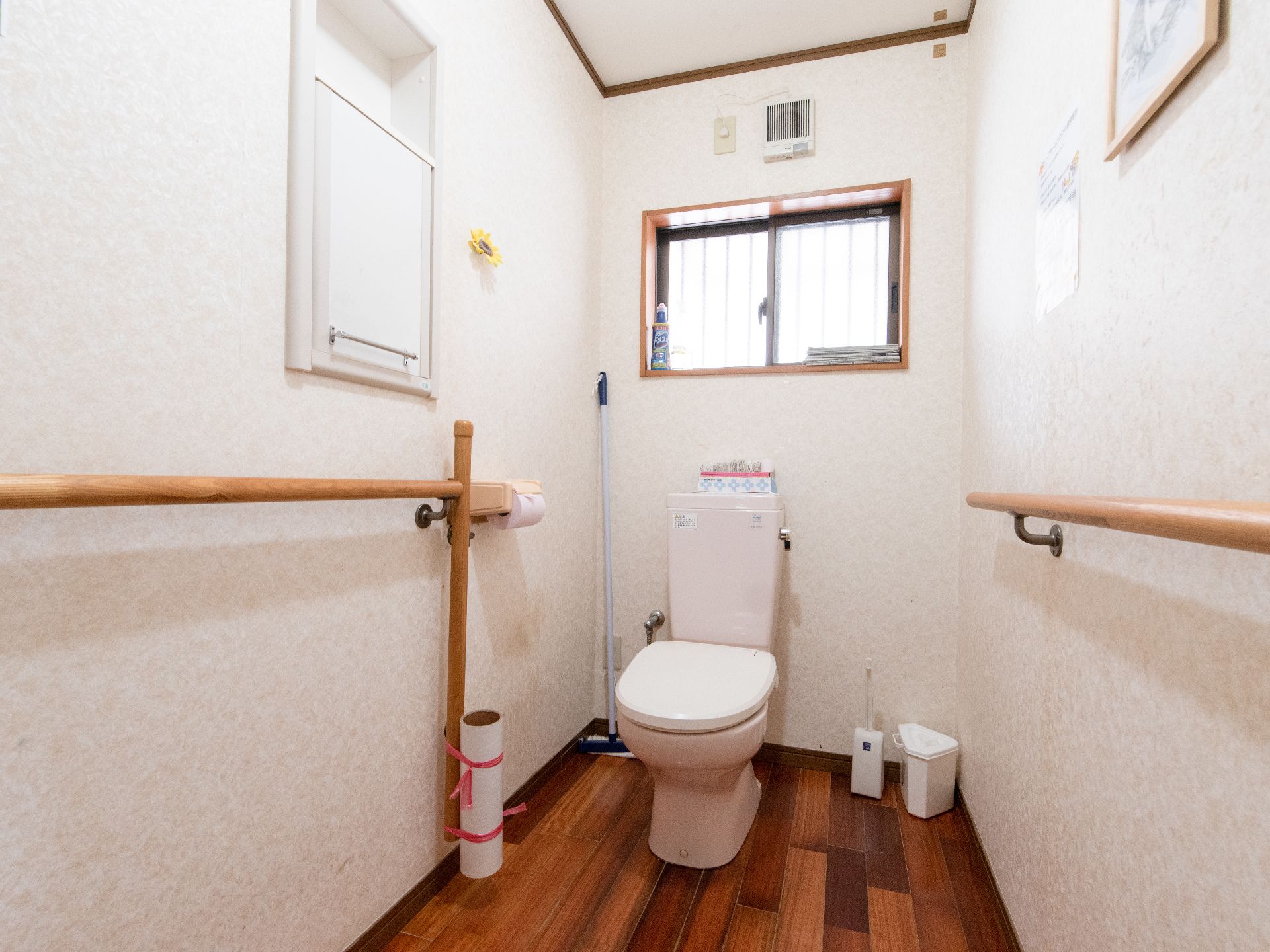 白を基調とした明るいトイレである。壁には収納棚が設置されているほか、手すりも両壁に取りつけられている。