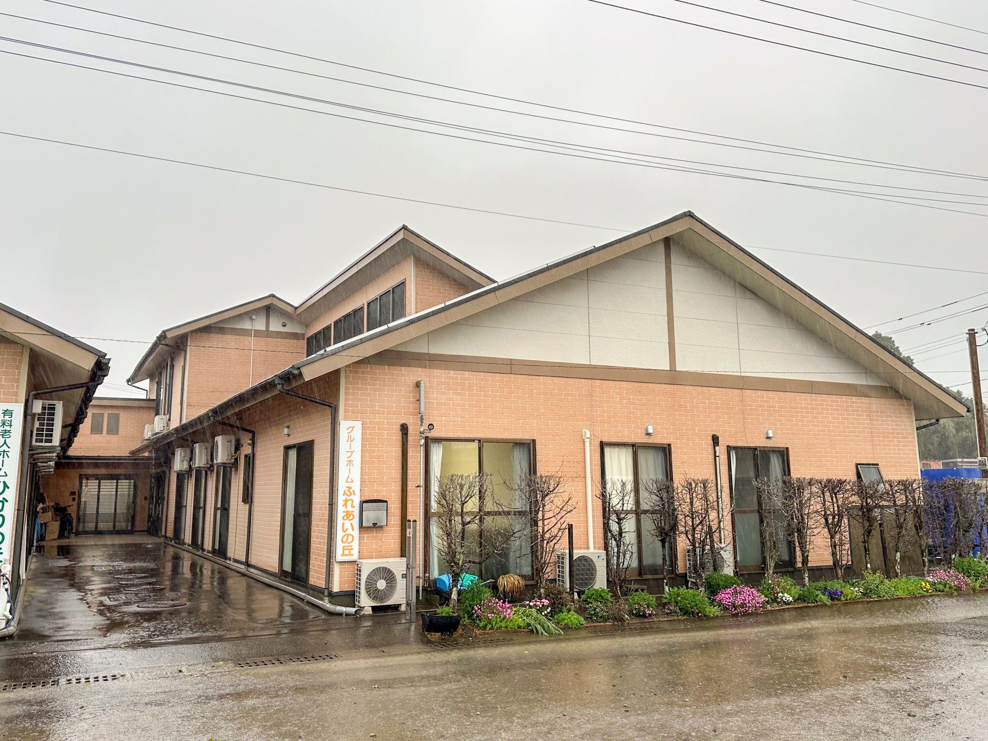 青い空の下に建っている平屋建ての建物の玄関先には屋根があり、屋根が付いた渡り廊下が続いている。