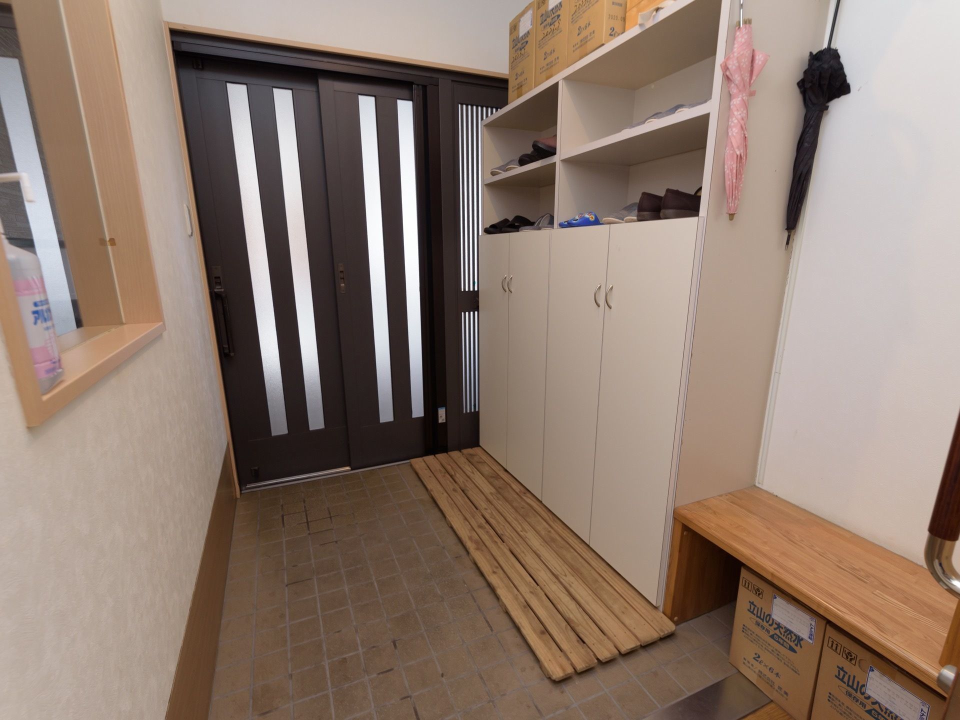入口の右手に天井近くまで届くサイズの白い下駄箱がある。両開きの扉と棚があり、たくさんの靴が置かれている。