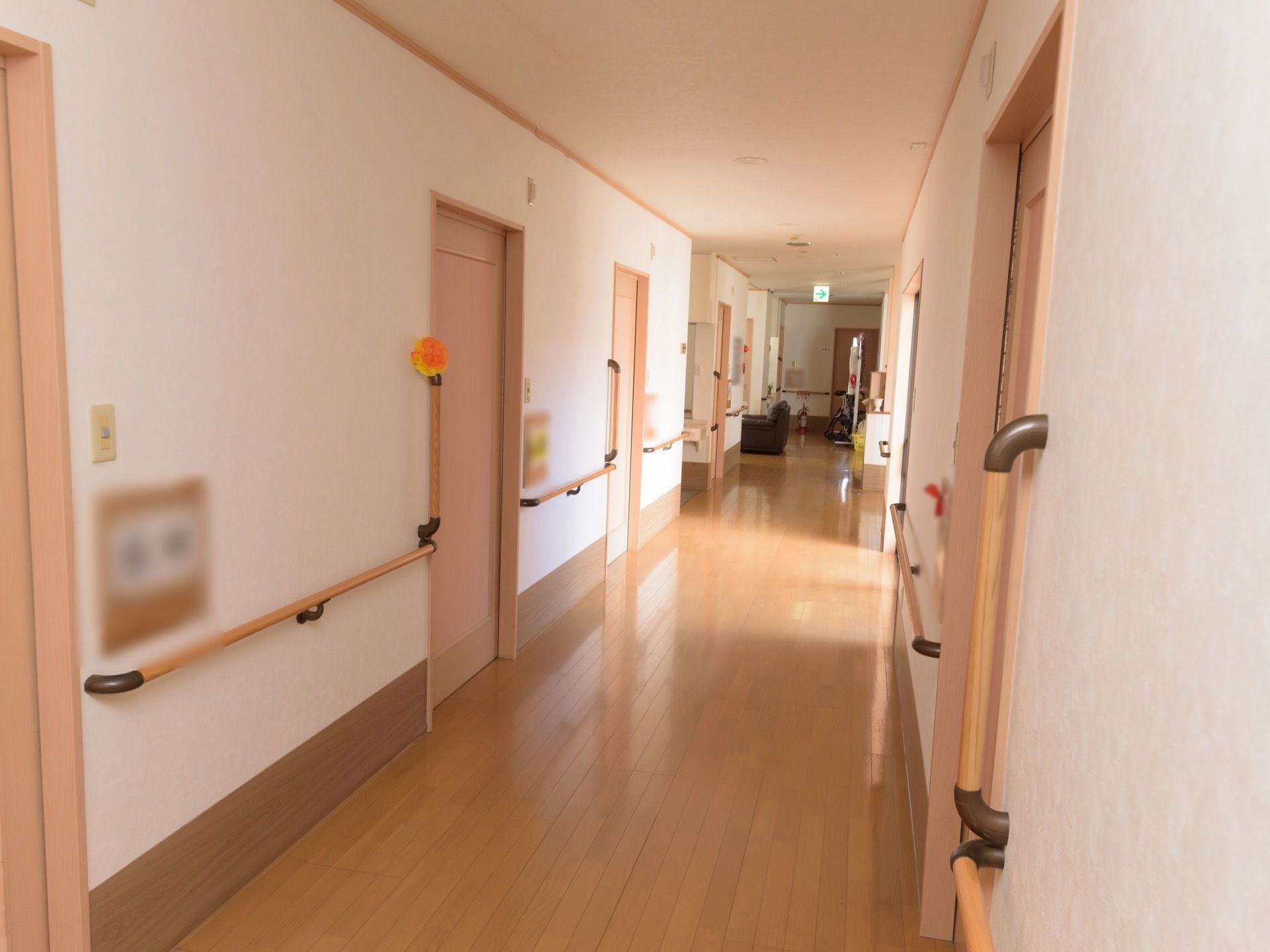 板張りの廊下が右奥に向かって真っすぐ伸びている。両側に居室へ続く引き戸が並んでいる。壁に手すりがある。