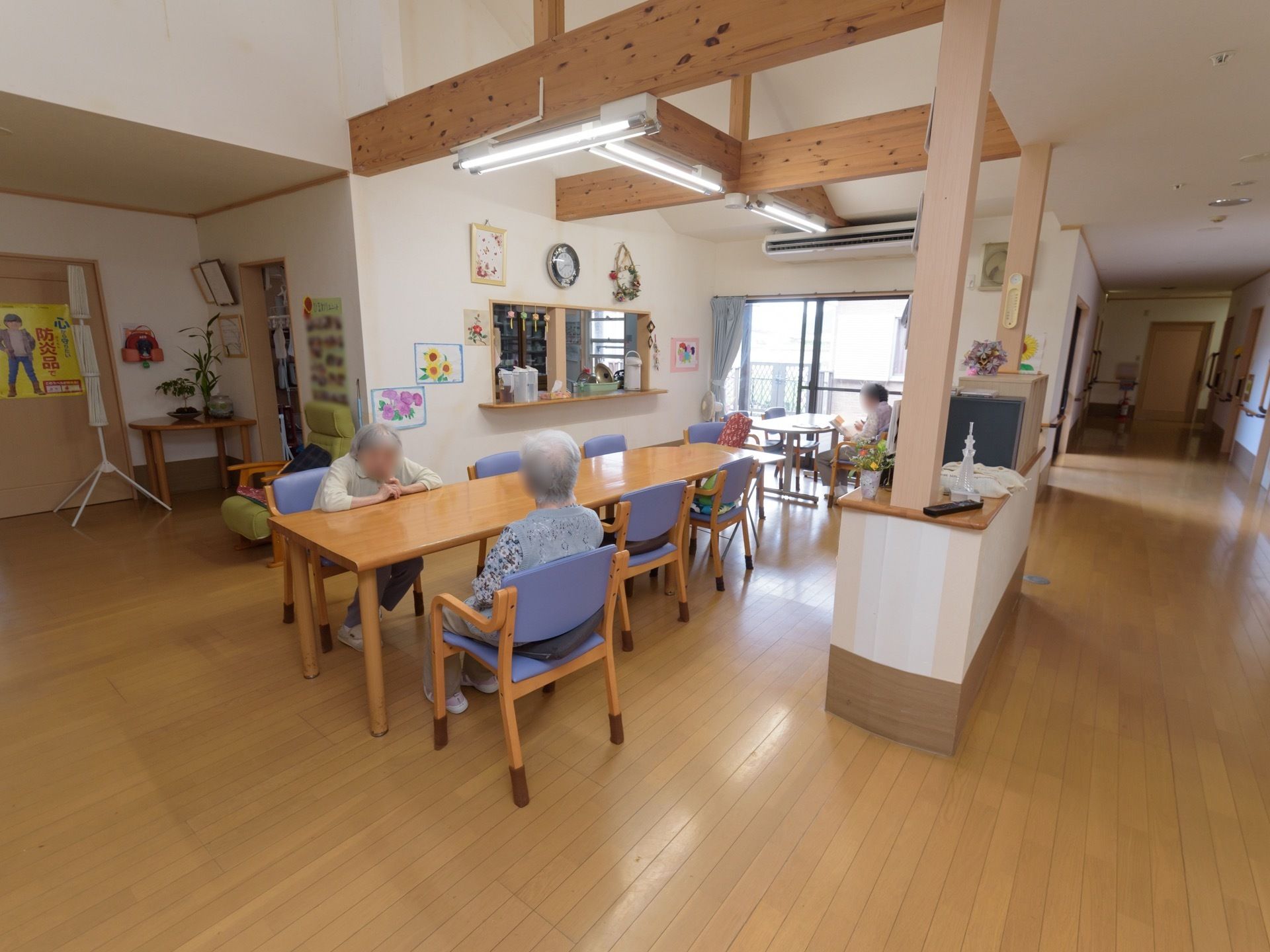 屋根まで吹き抜けになった共有スペースで、天井には太い梁が渡されている。中央にテーブルセットがある。