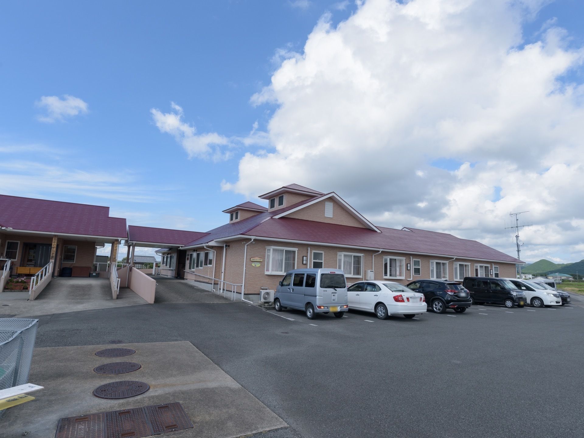 ベージュの外壁に、紫色の屋根が乗った平屋づくりの施設である。建物の前は駐車場があり、たくさんの自動車が停まっている。