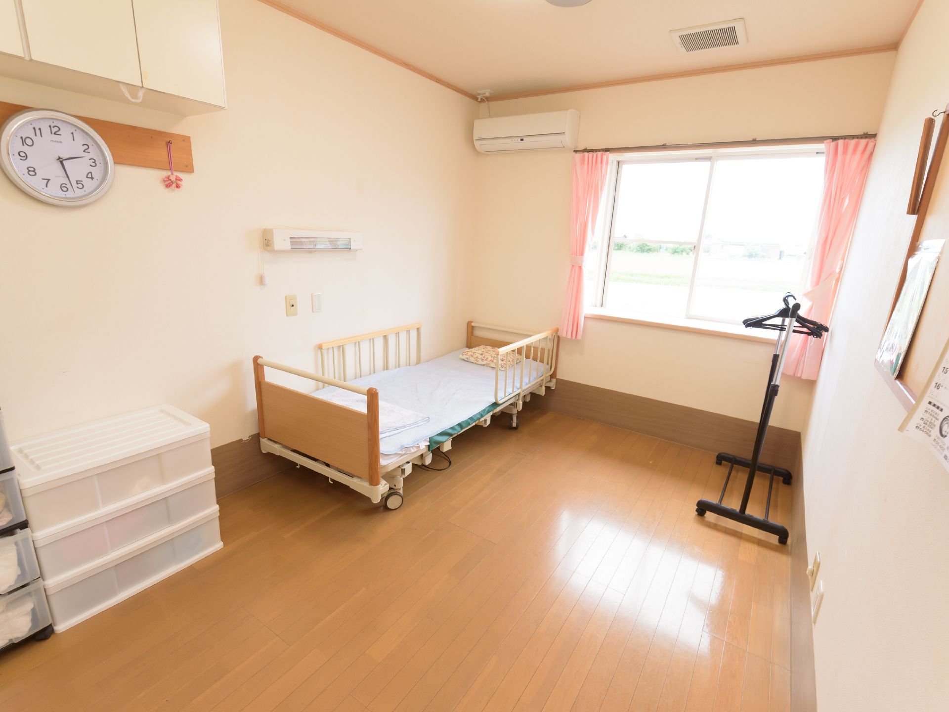 窓のそばにエアコンが設置され壁際に介護用ベッドが置かれた居室