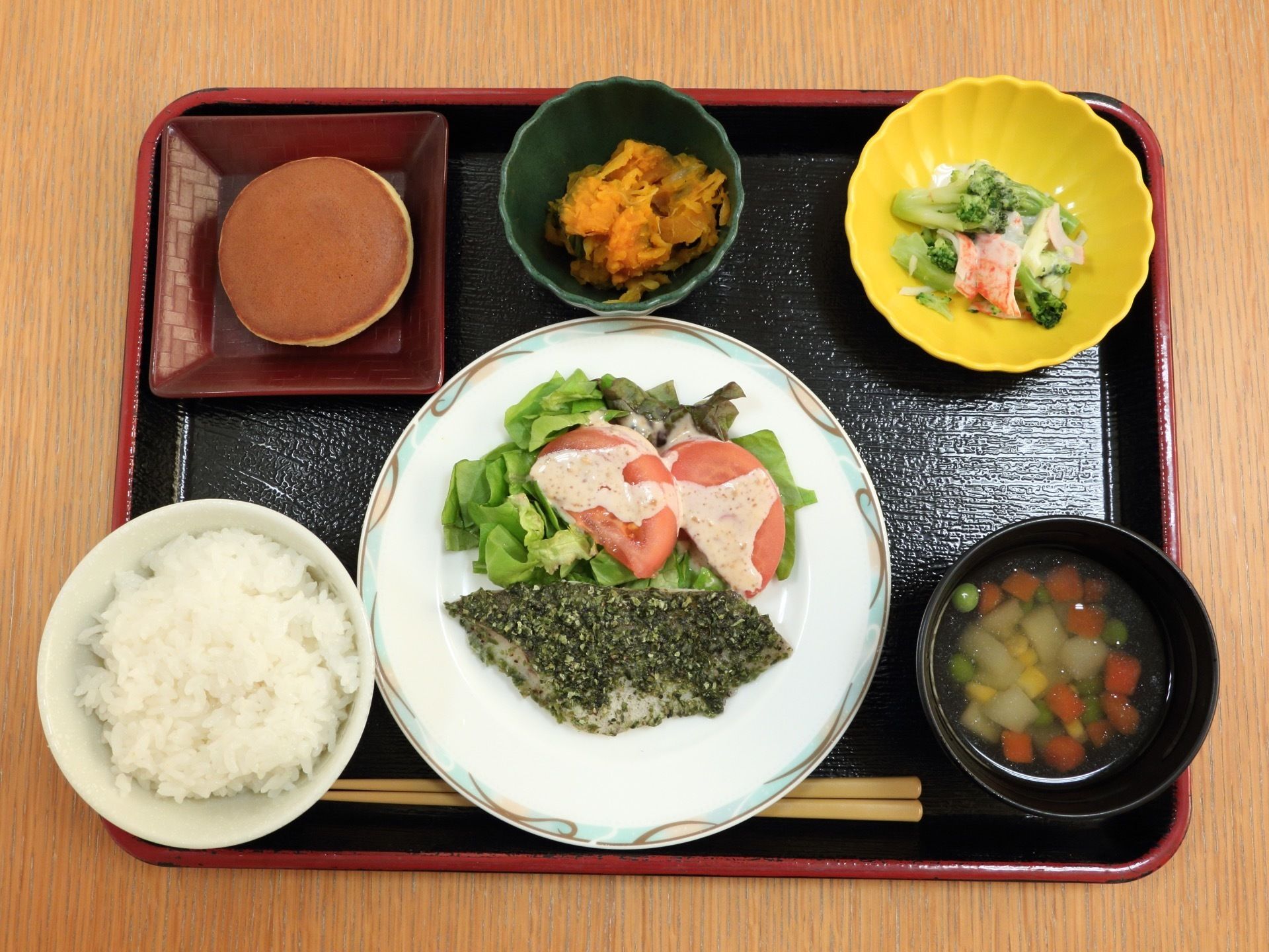 白身魚のハーブソテーと、トマトとレタスのサラダが、白い大きなお皿に盛り付けられている。その周りに、ご飯と汁物、煮物などがある。