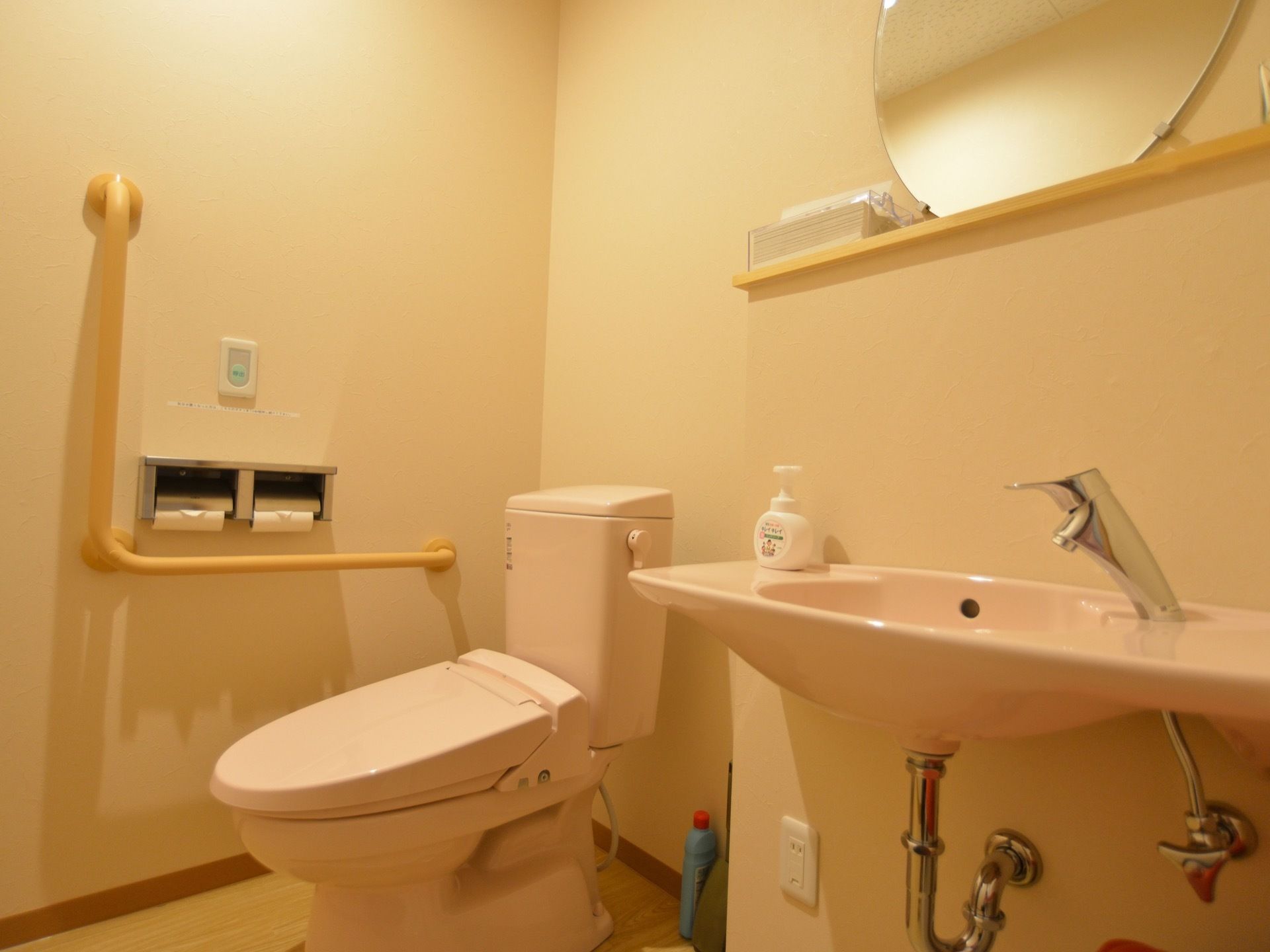 トイレ個室内の様子。奥にピンク色の洋式便器がある。その横にピンク色の洗面台がある。洗面台の上には、丸い鏡がある。