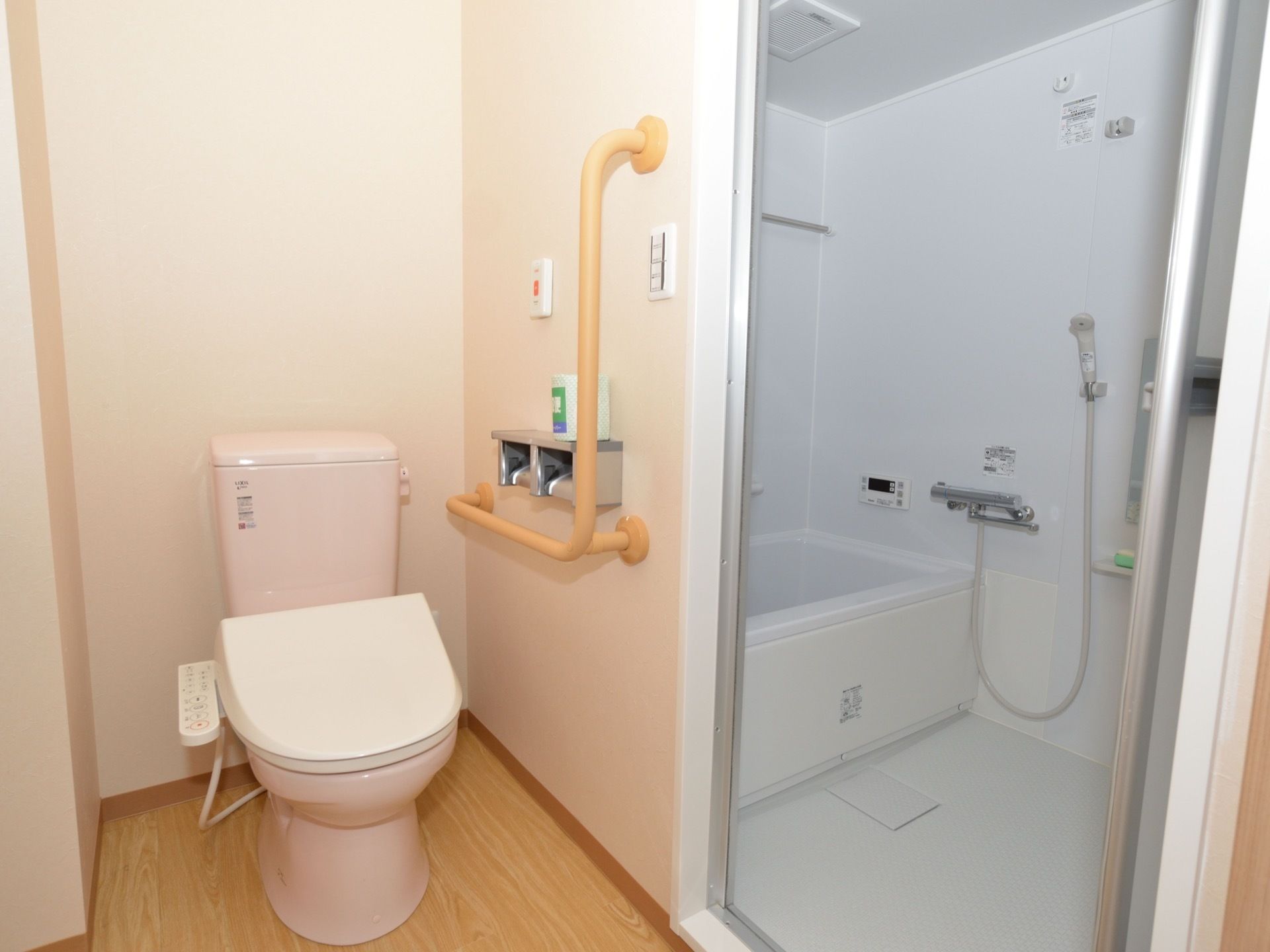 左側にトイレがあり、右側に浴室がある。トイレの壁にはL字型の手すりとナースコールが設置されている。浴室内には浴槽とシャワーが見える。
