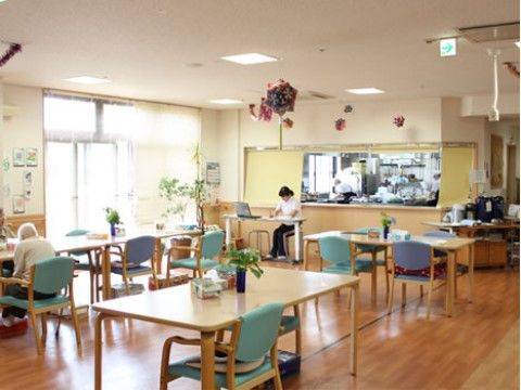 部屋にはテーブルと椅子が並んでおり、利用者様がくつろいで過ごしている。大きな窓があり、日当たりがよく明るい雰囲気である。