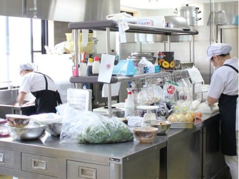 作業台の上には食材が並べられている。エプロン、マスク、帽子を着用している職員の姿がみられ、しっかりと衛生管理を行っていることがわかる。
