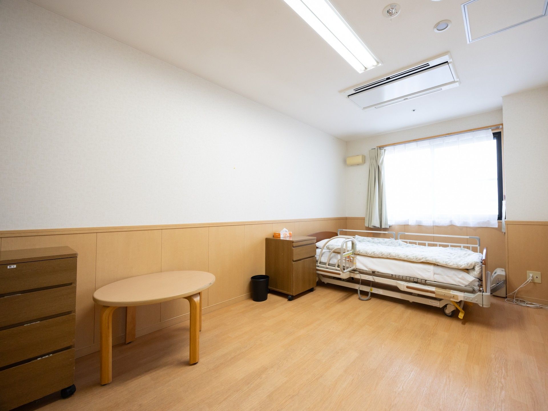 介護用ベッドに補助ホルダーが設置され窓際に置かれている居室