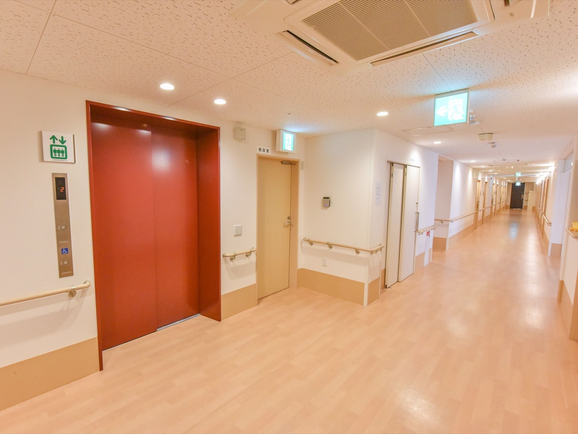 長く奥まで続く廊下には、入居者様用の居室と赤いドアのエレベーターがある。エレベーターの横には、階段へ繋がる扉もある。