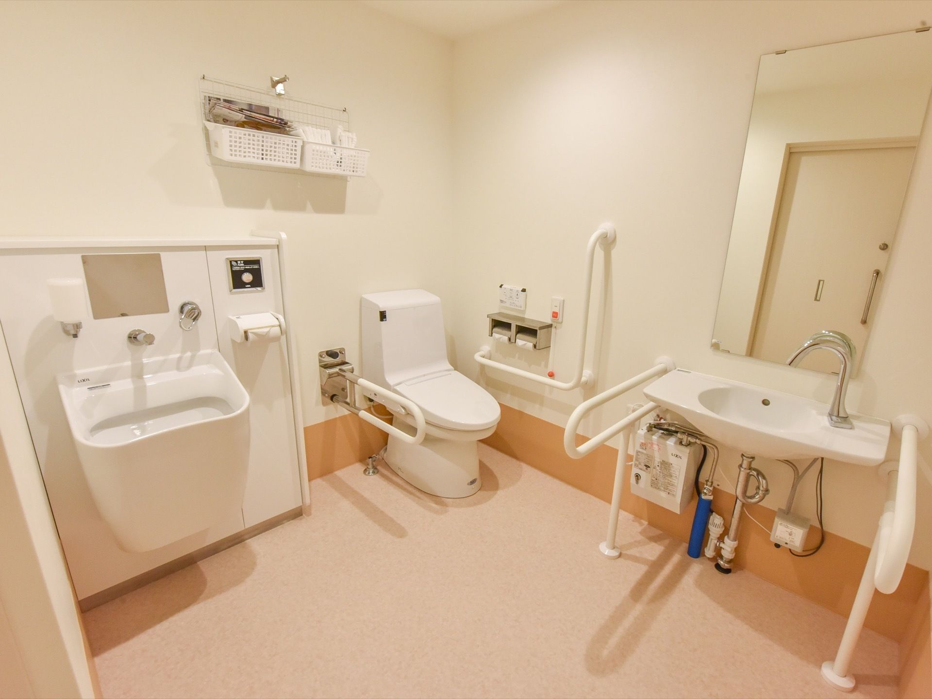 広々とした空間のトイレには、タンク付きのトイレと洗面台が2ヶ所設けられている。右側の洗面台には、手すりが取りつけられている。