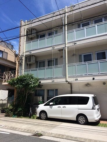 外壁側の駐車スペースに白い乗用車が停車している3階建ての施設