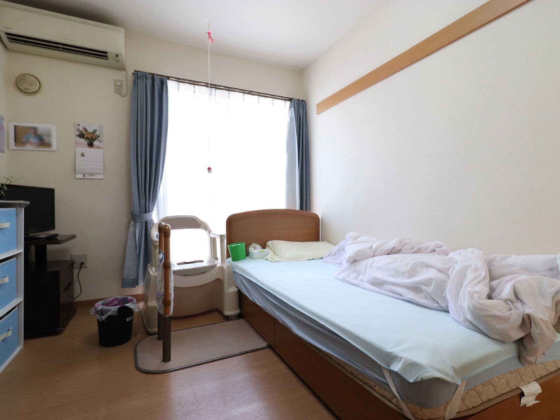 介護用ベッドのそばにポータブルトイレと自立型手すりが設置された居室