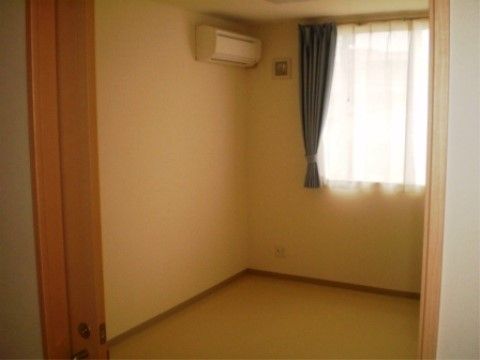 緑色のカーテンとレースカーテンが掛けられた窓から、柔らかな光が降り注いでいる。壁にエアコンが設置されている。