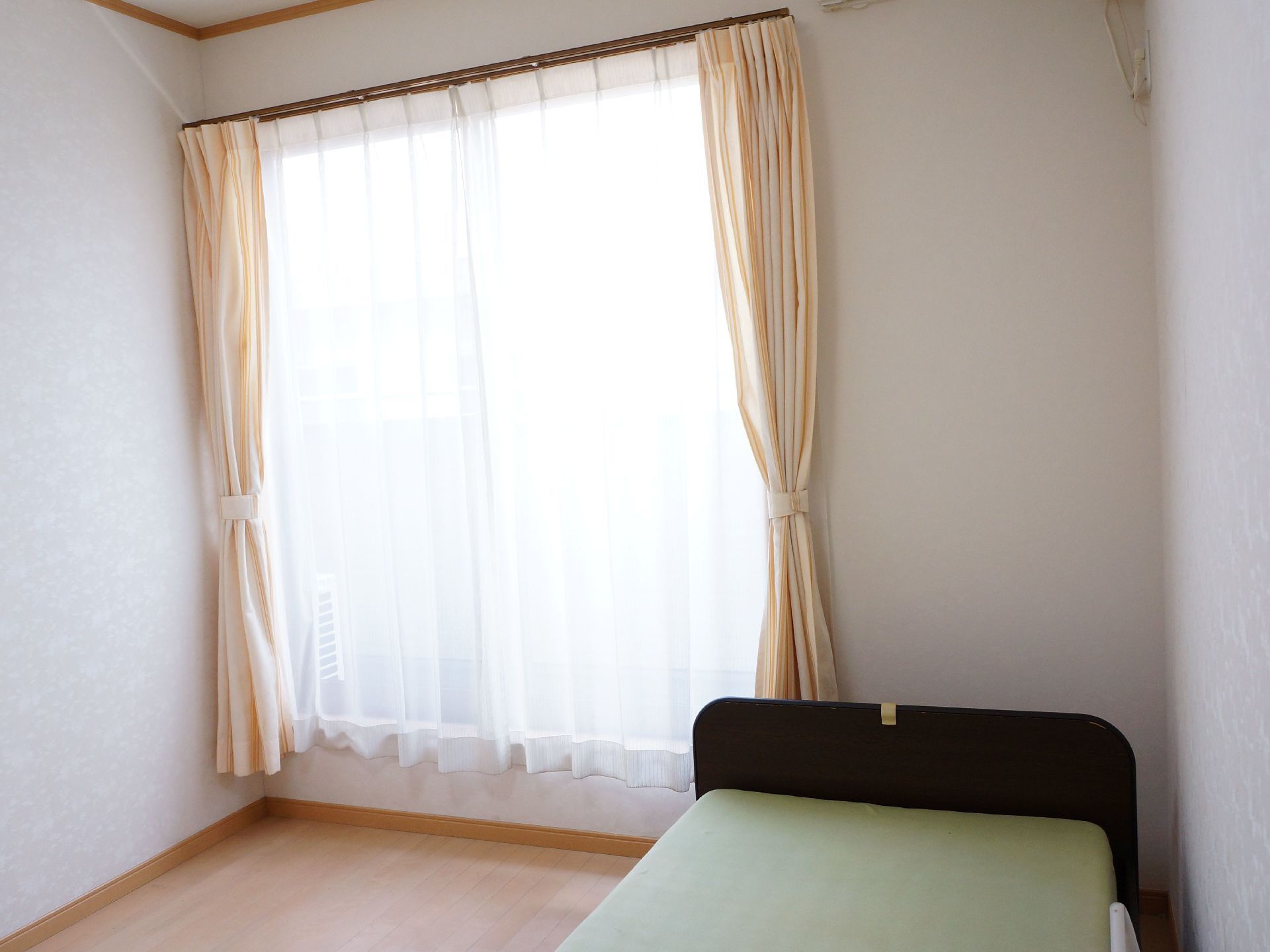 居室にはリクライニング機能がついた、介護用ベッドが置かれている。また室内には窓があり、カーテンが取り付けられている。