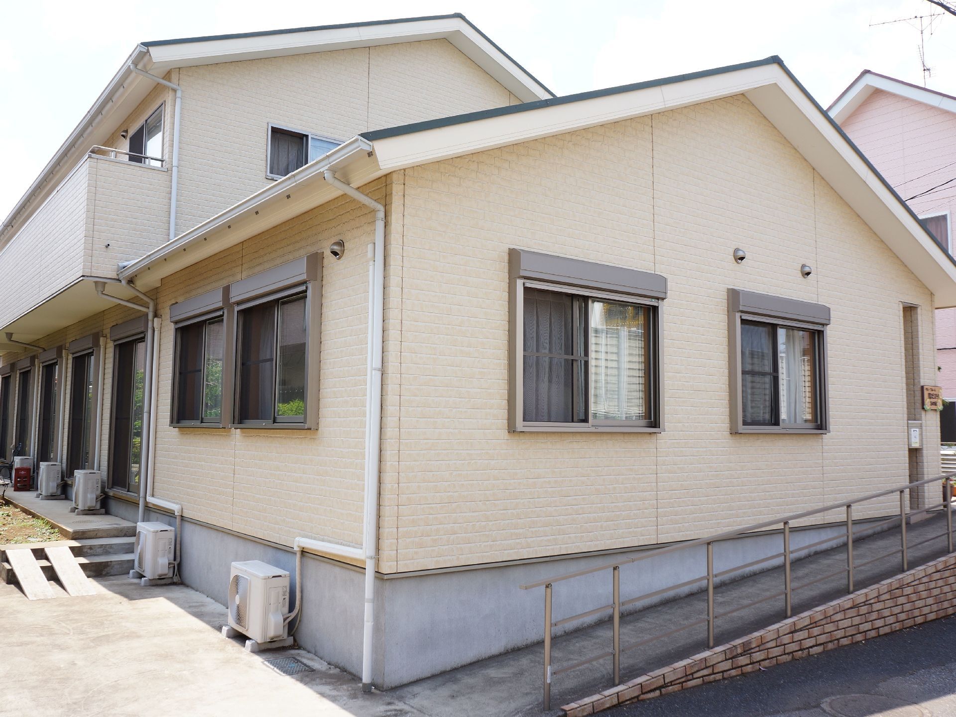 グループホームは２階建てで、ホワイトを基調とした外壁になっている。また入り口にはスロープと手すりが取り付けられている。
