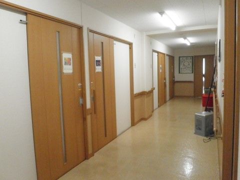 居室の扉は、横幅のある木製のスライド式のドアとなっている。縦長の小窓の横に、花の写真が印刷された紙が貼られている。