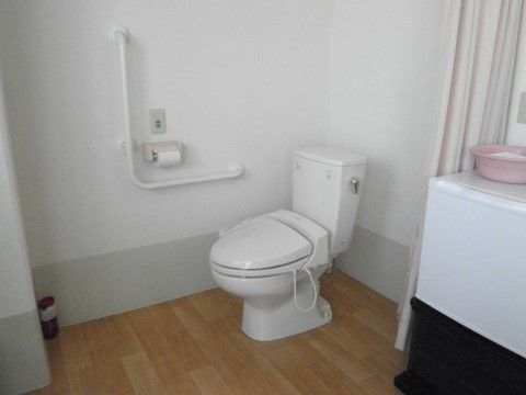 温水洗浄機能付きの洋式トイレである。壁にはＬ字型の手すりやペーパーホルダー、呼び出しボタンが設置されている。