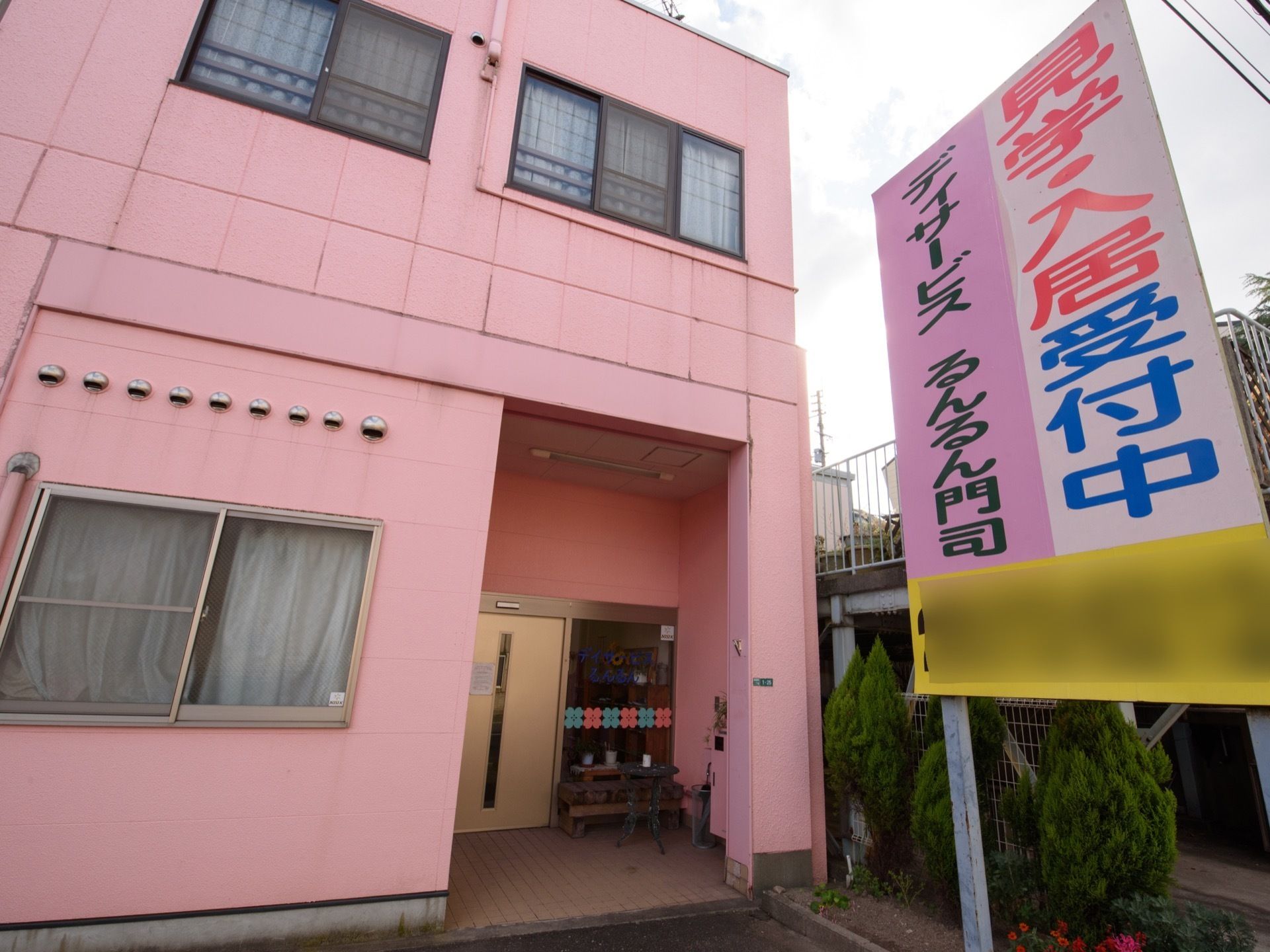 奥まったところに玄関があり、屋根がかかった状態である。建物の前には、施設名を表示した大きな看板が設置されている。
