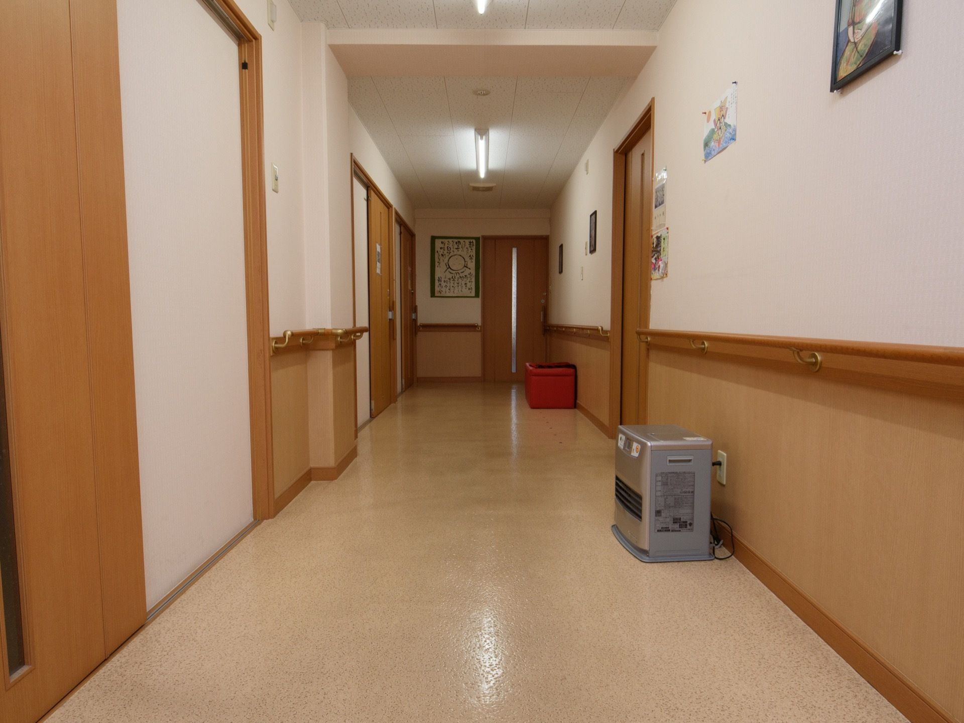 通路の壁は、手すりから上が白、下が木の色のツートンカラーである。えんじ色のスツールやヒーターが置かれている。