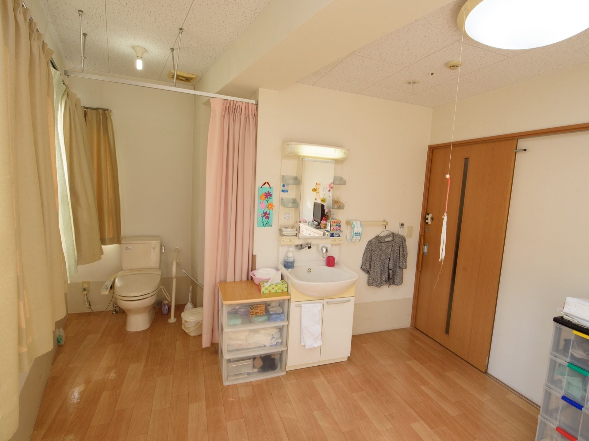 居室のトイレはカーテンで仕切ることができる。洗面化粧台のそばには、３段の収納ボックスが置かれている。