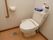 トイレは洋式で洗浄機能が搭載されている。トイレットペーパーフォルダの近くに手すりがある。トイレを清潔に保つための清掃道具が置かれている。