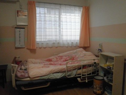ピンクの壁紙が柔らかい印象を与える。ベッドの側にはナースコールがついているので、24時間安心して生活する事ができる。