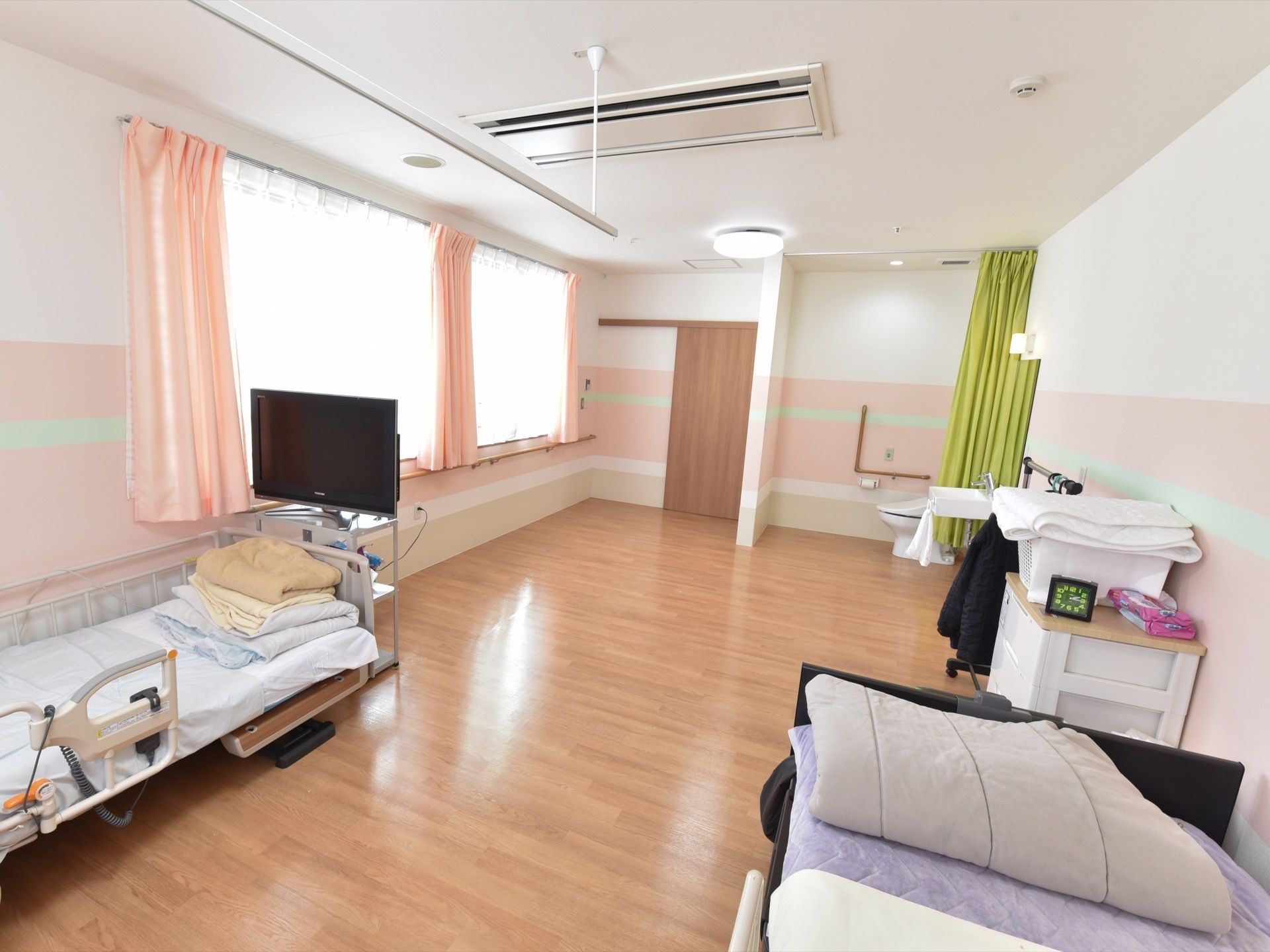 大きな窓がある、明るく広々とした多人数用の居室にはトイレと洗面スペースが設けられており、ベッドが２台置かれている。