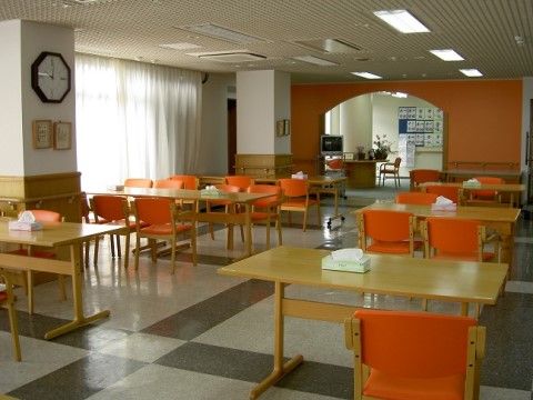 大きな窓から自然光が差し込んでいる。テーブルセットが２列に並び、アーチ形の仕切りの奥には展示作品が見える。