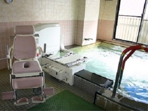 タイル張りの大浴場の窓からの光を、大きな浴槽の湯が反射している。床には滑り止めのマットが敷かれ、リフト入浴機器も置いてある。