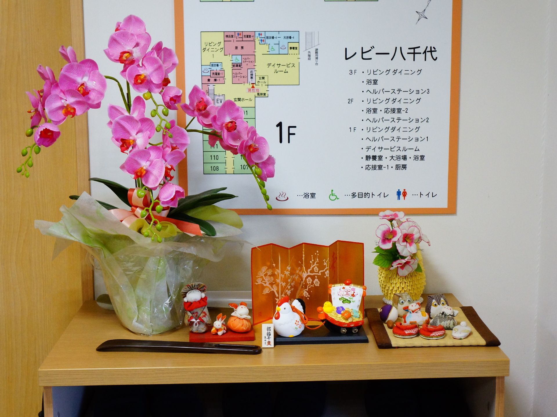 壁には館内の配置を知ることができるフロア案内図を設置。手前にはランの花や、干支の人形などが置かれている。