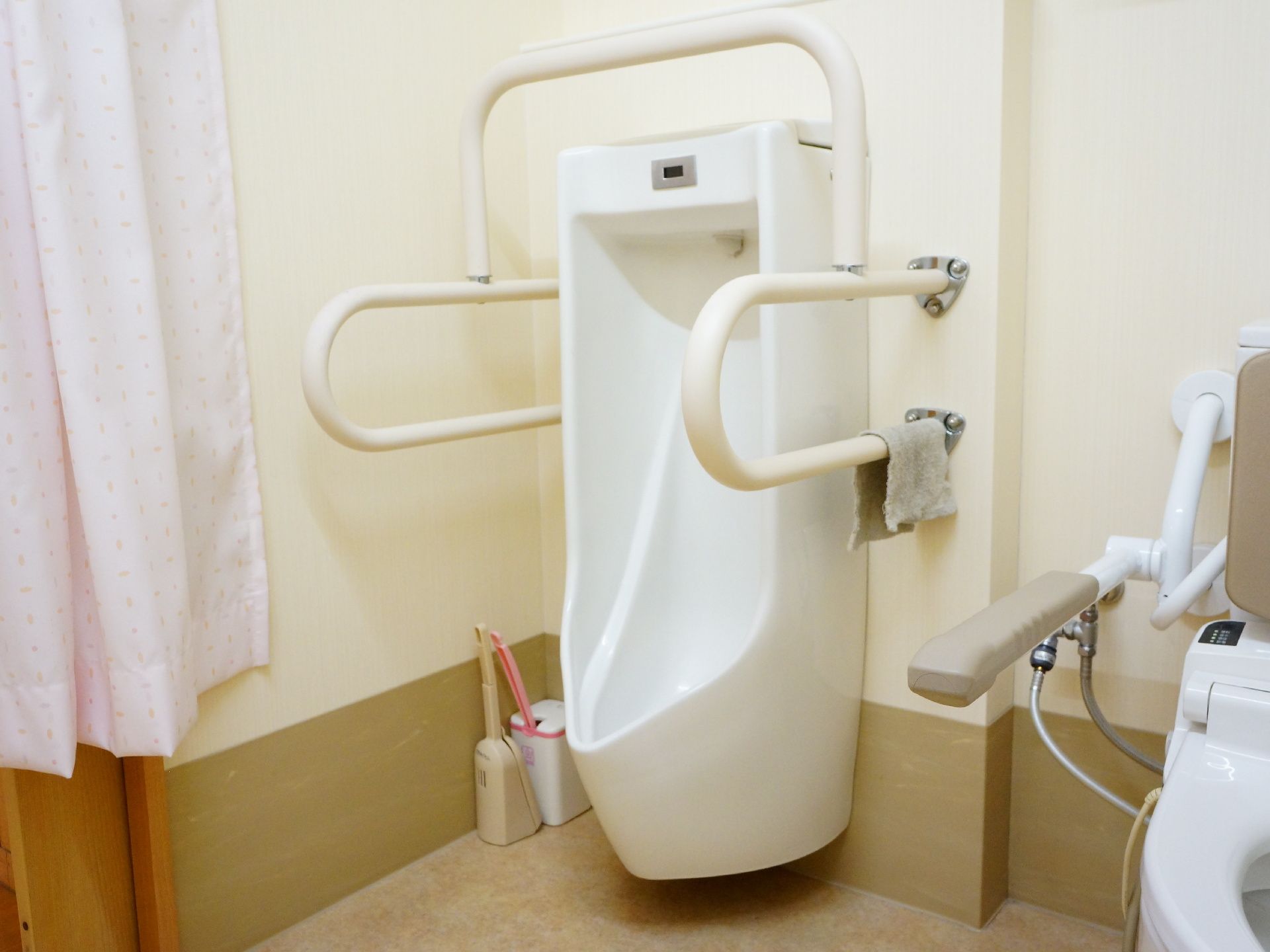 手すりがあれば立って排泄ができる方のため、男性用小便器がある。便器の両側と上部に、白いしっかりとした手すりが備え付けられている。