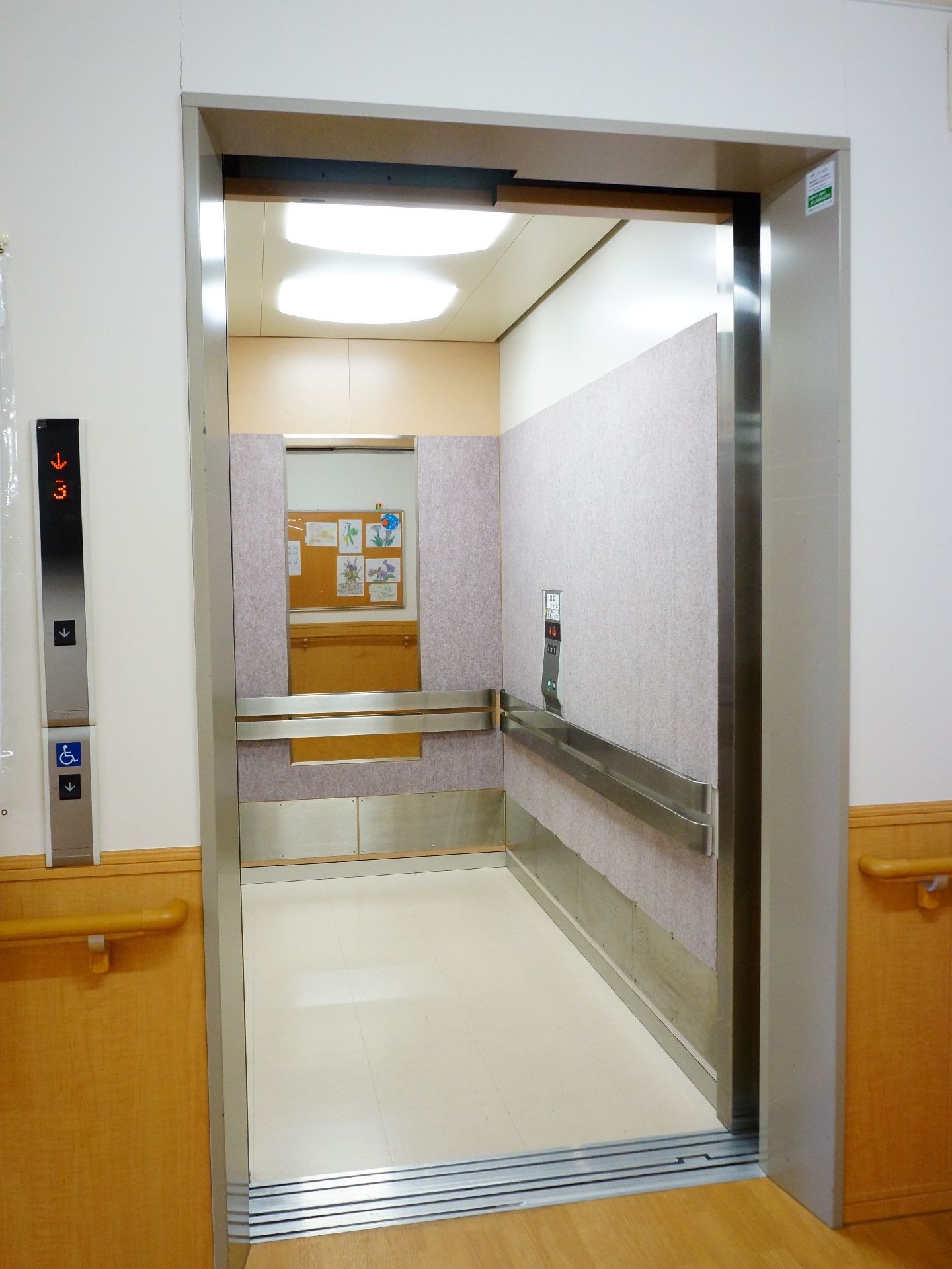 エレベーター内は奥行きが深く細長い。壁面には手すりが、奥には鏡が設置されている。天井には電気が2つついており、中を明るく照らしている。