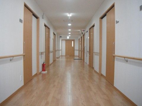 一直線上の廊下は明るく、横幅も十分に確保されている。入居者様の居室が壁の両側に並んでいるほか、廊下の中央付近にはトイレが配備されている。