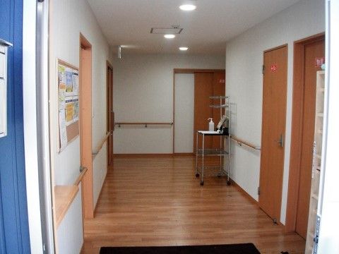 フローリングが照明に照らされた、明るい雰囲気のエントランスである。壁には手すりが設置されているほか、来訪者様向けの掲示物が張られている。