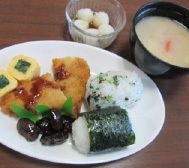 俵型おにぎりと黒豆や卵焼きやフライに味噌汁がセットになったメニュー