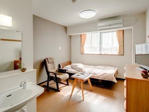 白を基調とした明るい部屋である。床はフローリングになっている。洗面台やチェストの上には花が飾られている。